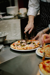 Chef cutting pizza with the round pizza cutter or knife.