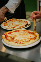 Chef smears olive oil to the top of pizza.