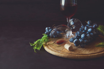 Two wineglasses with red wine and grapes decorated vine leaves on dark wooden desk