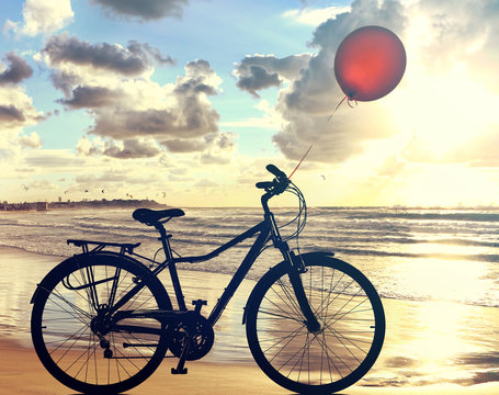 Bike lonely is on wet sea sand of the beach against the backdrop of beautiful seaside at sunset. Red balloon is flying up. Leisure and sport. Adventure and dreams