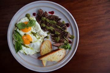 Grilled beef steak with toast , fried egg and vegetables on top with pesto sauce