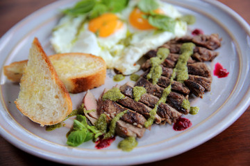 Grilled beef steak with toast , fried egg and vegetables on top with pesto sauce