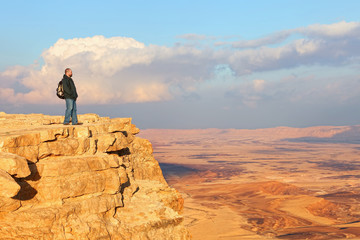 Traveler (hiker man) on a mountain edge top. Colored sand stone desert under beautiful sky before sunset. Unique geological erosion land form. National park Makhtesh Ramon (Crater). Negev, Israel © Alexey Protasov