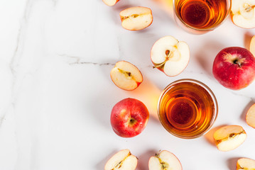 Fresh organic farm apple juice in glasses with raw whole and sliced red apples, on white marble table, copy space top view