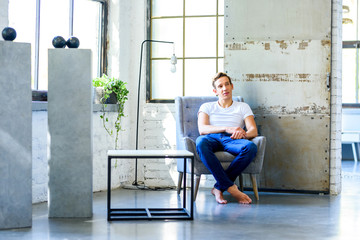 A young handsome man relaxing in a armchair in a loft style apar