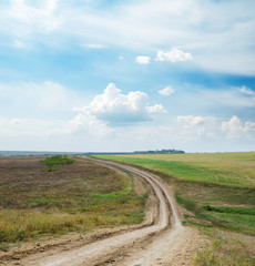Fototapeta premium dirty road in field and blue sky with clouds
