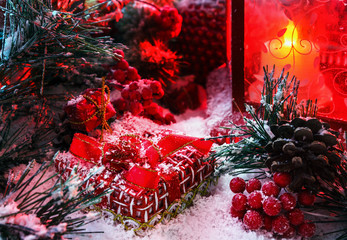 Christmas gift covered with snow in the light of a red lantern on the background of New Year's scenery
