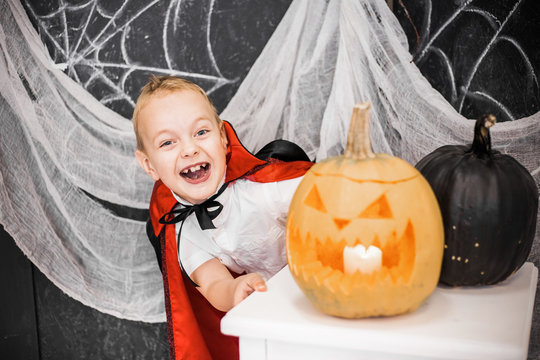 Portrait Of Funny Emotional Little Boy With Cute Toothless Smile. Cheerful White Child Playing In Costume Of Vampire In Beautiful Halloween. Festive Decor In Black And White Colors.