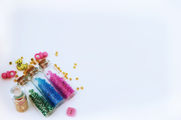Tiny glass bottles filled with  colored  beads and elements for baby  spilling out, isolated on a white background with space for text. 