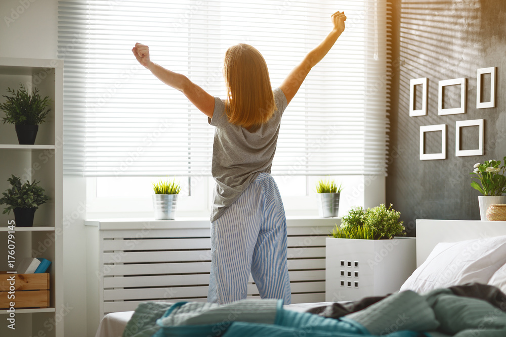 Poster young woman woke up in the morning in the bedroom by the window with her back.