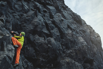 male rock climber. rock climber climbs on a black rocky wall on the ocean bank in Iceland, Kirkjufjara beach. man makes hard move without rope.