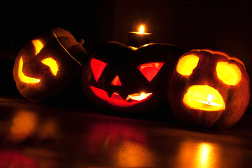 Scary halloween pumpkin and melon jack-o-lanterns on black background lit with small round and star candles