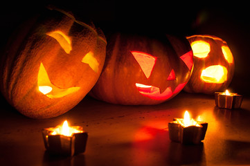 Scary halloween pumpkin and melon jack-o-lanterns on black background lit with small round and star candles
