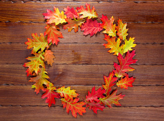 Autumn background with yellow, red and bright leaves. Round frame of autumn foliage on the old wood with free space. The layout offers and seasonal holiday card