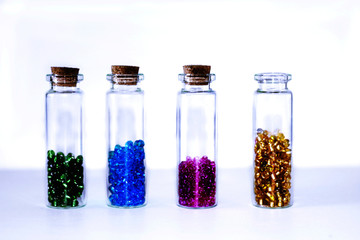 Little glass bottles with colored seed beads inside isolated on white background.