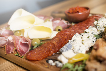 Mediterranean olives, sun-dried tomatoes, baguette slices, camembert cheese and spices on wooden background. Sausage and prosciutto slices on a wooden board. Appetizers served at an event.
