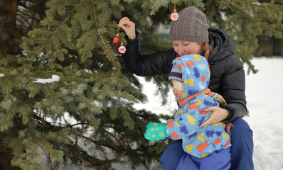 A mother and her child decorate the Christmas tree on the street in winter