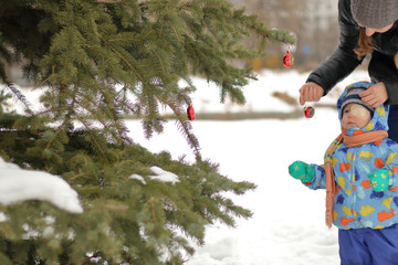A mother and her child decorate the Christmas tree on the street in winter