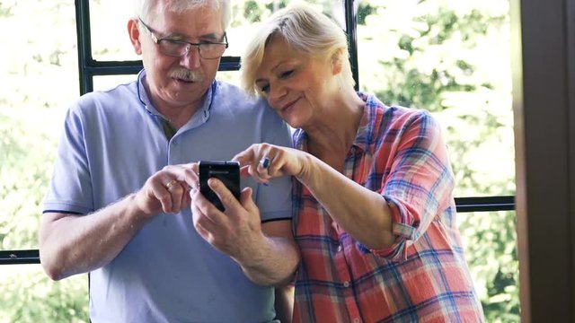 Mature couple talking and using smartphone sitting by the window
