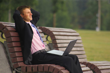 Fototapeta premium Young businessman is sitting at the park and using laptop