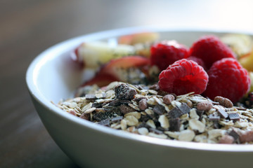 mixed fruit and cereal in a white bowl on brown wooden table