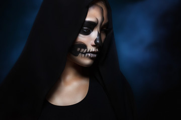 Halloween portrait of young beautiful girl in a black hood. skeleton makeup half face