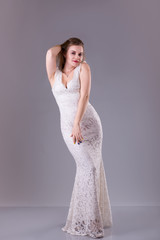 Fototapeta premium Curvy model with long hair, red lips wearing evening white dress. Plus size woman fashion.