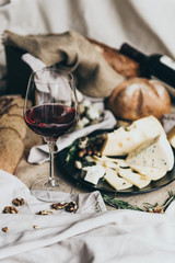 A wineglass is filled with dry red wine lying behind. Fresh bread, blue cheese, masdaam cheese,...
