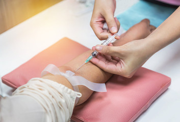 Nurse injecting with syringe to patient's arm drawing blood sample for blood test in hospital