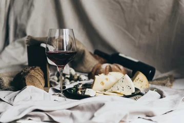 Fototapeten A wineglass is filled with dry red wine lying behind. Fresh bread, blue cheese, masdaam cheese, quail eggs and nuts are used as decoration. © Studia Nizhny