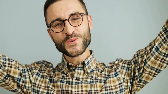 Close up shot of a young caucasian man in a casual shirt rising both hands and showing satisfaction and greay joy on the grey background. Outdoor shot.
