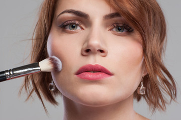 Beauty style. Female nude blush makeup tutorial. Young woman with face paint on grey background. Modern pretty girl with clean skin closeup