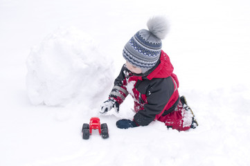 Fototapeta na wymiar A child sculpts a snowman in the winter on the street, a boy in a red overall