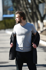 Fototapeta premium Guy with beard and haircut in grey tshirt undressing coat