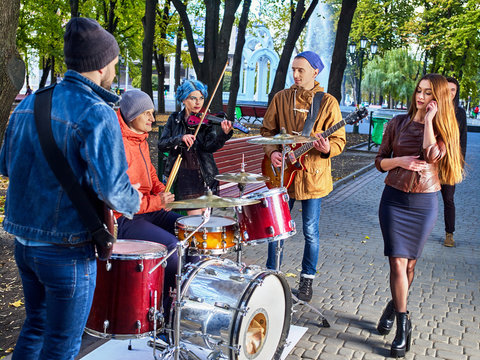 Festival music band. Friends playing on percussion instruments in city park. Fountain and trees in the background. People earn money to live.