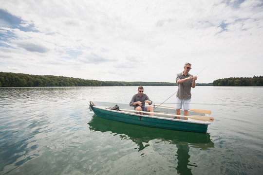 Two caucasian men are preparing their equipment for fly fishing from a boat on lake.