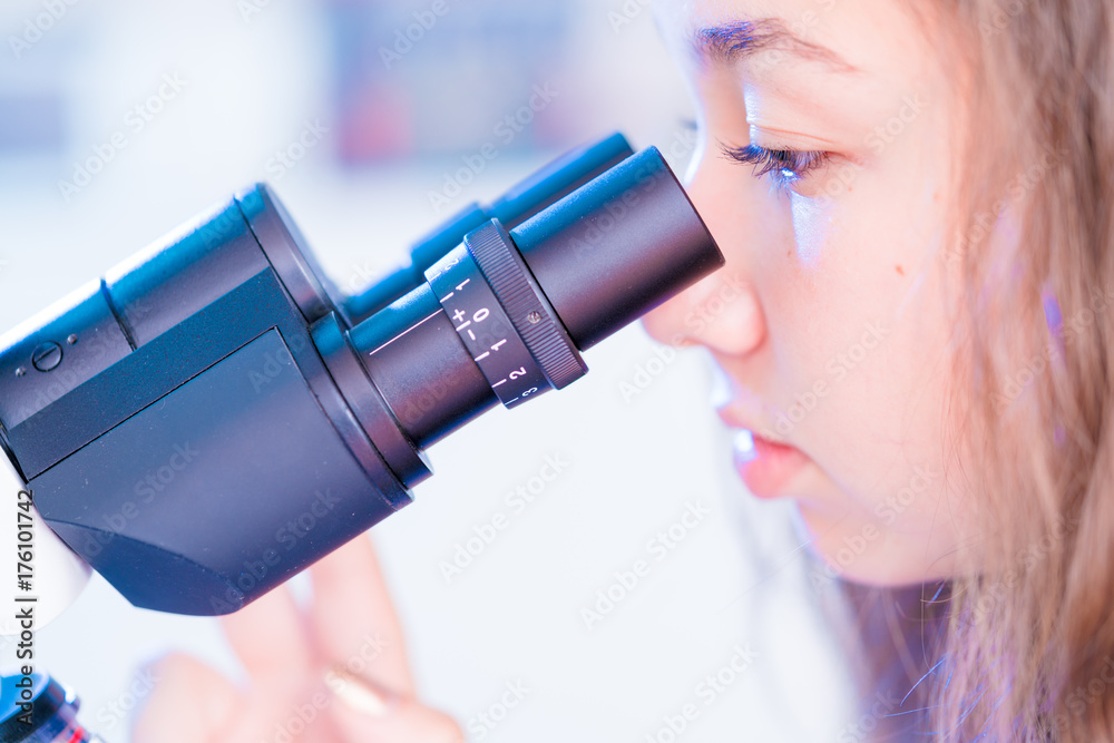 Sticker schoolgirl girl looks through a microscope at a biology class at a gymnasium