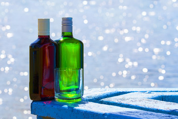 Bottles of whiskey and gin with glass on background of lake