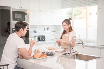 Man drinks coffee while a woman prepares a meal