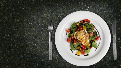 Grilled Halloumi Cheese poured with garlic olive oil salad witch grilled eggplant, cherry tomatoes, black olives and spinach. healthy food. Top view on granite kitchen countertop. Copy space added.