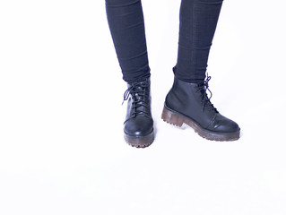 Closeup of woman wearing black skinny jeans and black faux leather biker boots with chunky sole isolated on white background. Copy space.