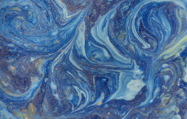 Marbled blue abstract background with golden sequins. Liquid marble ink pattern.