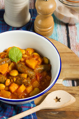 Butternut squash, pumpkin and bean stew with beef sausages. White bowl, dark blue tablecloth, wooden board.