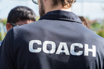 back of a sport coach's black shirt with the white Coach word written on it