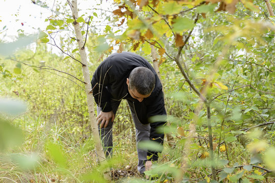 man with short hair and black clothes bent over the find in the woods