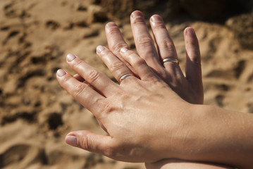 Man and Woman holding Hands with a Wedding Rings on Sand Background