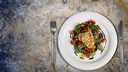 Grilled Halloumi Cheese poured with garlic olive oil salad witch grilled eggplant, cherry tomatoes, black olives and spinach. healthy food. Top view on granite kitchen countertop. Copy space added.