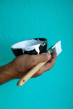 Man Holding A Paint Brush And A Bowl Of White Paint Against A Colorful Wall