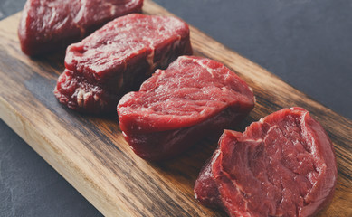 Raw beef filet mignon steaks on wooden board at gray background