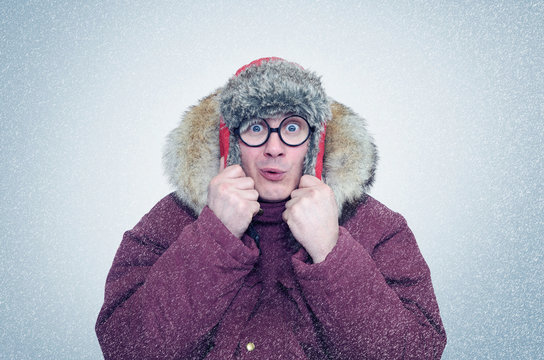 Frozen man in glasses and winter clothes warming ears, cold, snow, blizzard